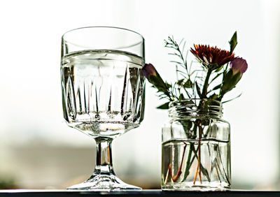 Glass of water and small bouquet of flowers in jar close-up in sun back light, healthy lifestyle