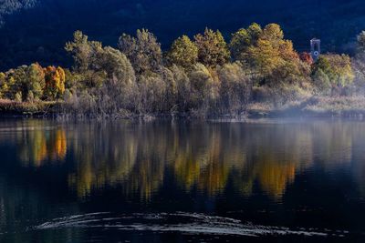Trees by lake against sky during autumn