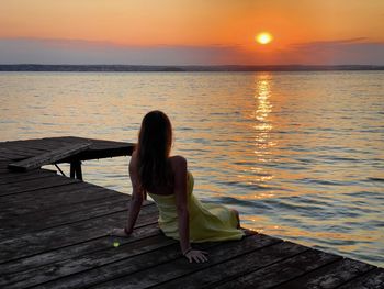 Woman sitting down on a wooden pontoon over the lake and enjoying the sunset