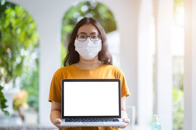 Portrait of woman wearing mask holding laptop