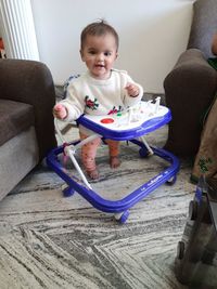 Portrait of cute baby girl standing in walker at home
