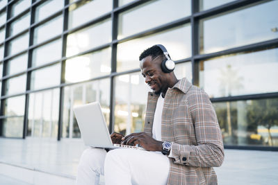 Man using laptop while listening to music against building