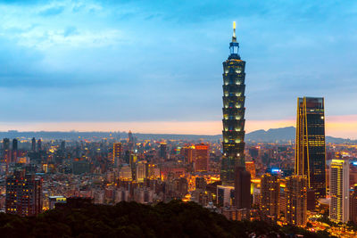 Illuminated buildings in city against cloudy sky