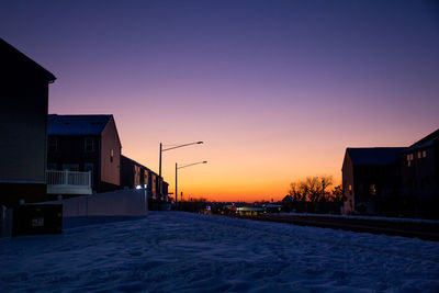 Snow covered buildings against sky during sunset