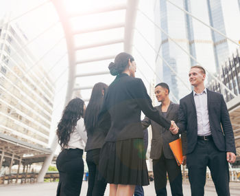 Business people giving handshake while standing against building in city