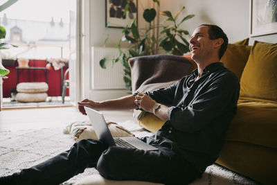 Male entrepreneur laughing while sitting with laptop in living room