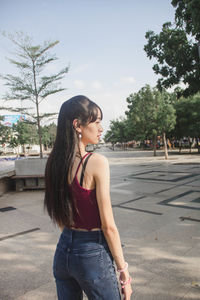 Young woman looking away while standing by tree in city