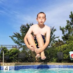 Low angle view of boy jumping in swimming pool against sky