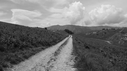 Dirt road amidst field against sky