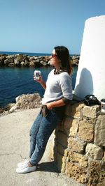 Young woman holding coffee cup while standing on footpath at coral bay beach