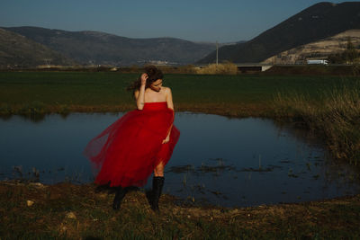 Young female model posing at lakeshore against mountains