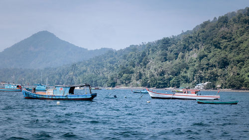 Boats sailing in sea against mountains