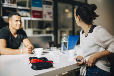 Businesswoman injecting insulin while talking to colleague at table