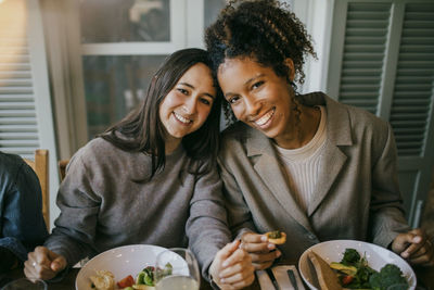 Portrait of smiling young female friends sitting at dining table in patio for dinner party