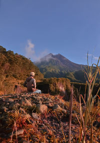 Man sitting on field against mountain range against clear sky