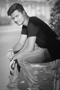 Side view portrait of young man sitting on retaining wall at footpath