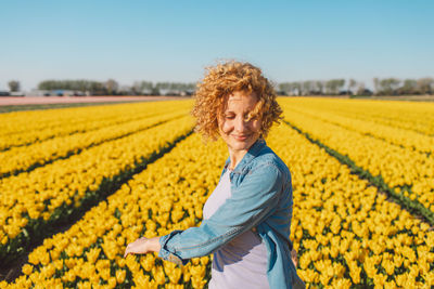 Portrait of woman standing amidst yellow flowering plants on field against sky