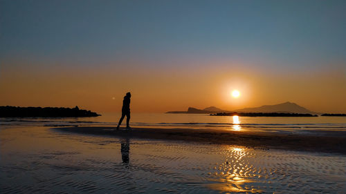 Silhouette person on beach against sky during sunset