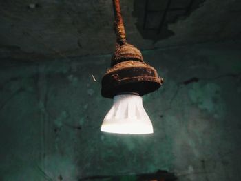 Low angle view of illuminated light bulb hanging on wall
