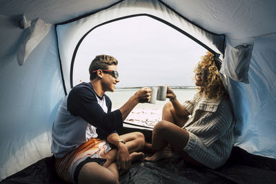 Young couple sitting on chair by water against sky