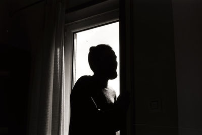 Silhouette man looking through window at home
