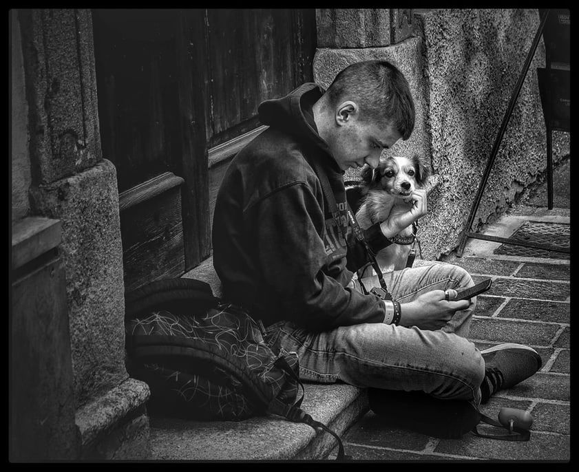 REAR VIEW OF MAN SITTING WITH DOG ON STREET