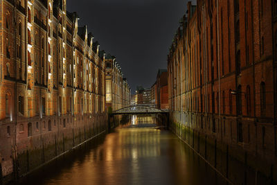 Bridge over canal amidst buildings in city at night