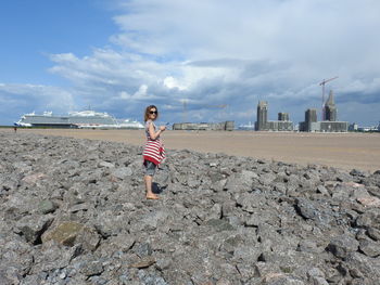 Full length of girl standing on rock at beach against sky