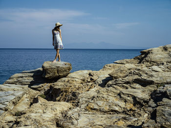 Man standing on rock by sea against sky