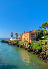 Buildings by sea against clear blue sky