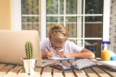 Rear view of boy sitting on table at home