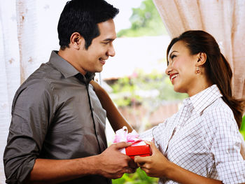 Smiling mid adult man giving gift to girlfriend at home