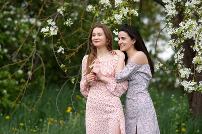 Two young girls in dresses are standing under a white tree laughing and looking away