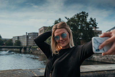 Smiling young woman taking selfie while standing in city