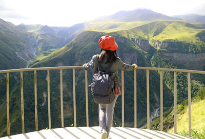 Rear view of woman standing by railing against mountain