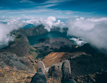 Low section of man standing on rock against sky