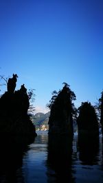 Silhouette trees by lake against clear blue sky