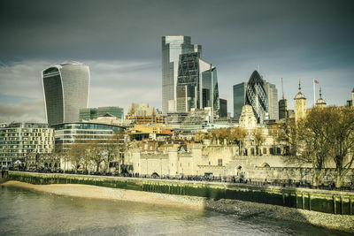 Modern buildings by river against sky in city