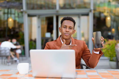 Portrait of businessman showing smart phone at cafe