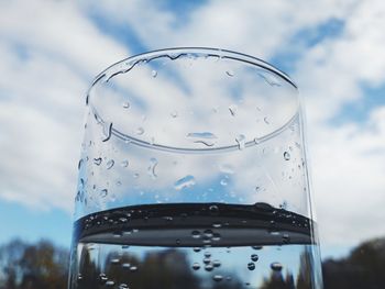 Close-up of water drops on glass against sky