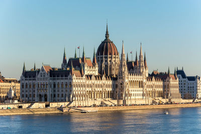 Hungarian parliament building by danube river against clear blue sky
