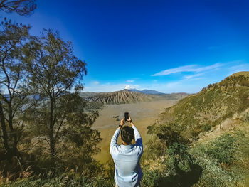 Rear view of woman standing on mountain against clear blue sky