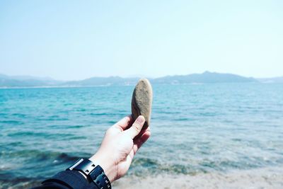 Cropped hand of woman holding stone over sea against sky