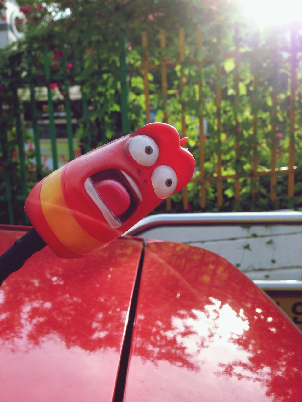 red, close-up, focus on foreground, single object, day, part of, no people, sunlight, metal, toy, still life, outdoors, tree, transportation, protection, heart shape, safety, animal representation, pole, plastic