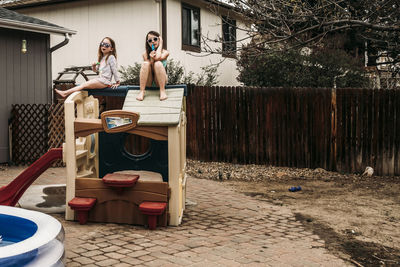 Sisters having popsicles while sitting on outdoor play equipment at backyard
