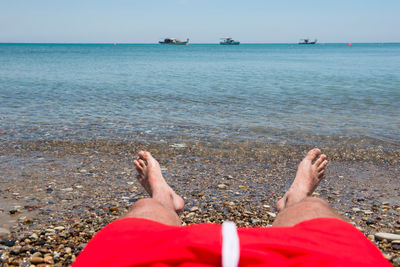 Low section of man relaxing on shore at beach