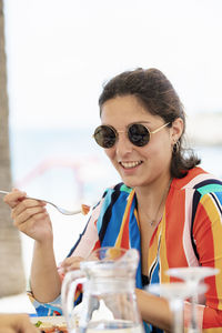 Portrait of smiling young woman holding sunglasses