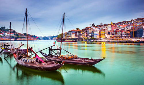 Sailboats moored on river by buildings against sky in city