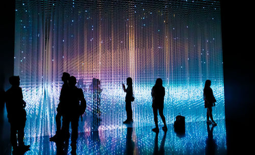 Silhouette people standing in illuminated water at night