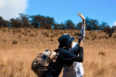 Rear view of man with arms raised on field against sky